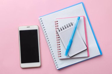 Hassas pembe arka planda not defterleri ve akıllı telefonlar. en üstteki görünüm