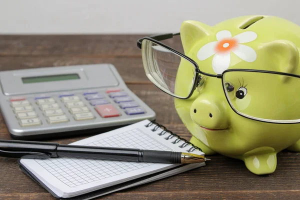 green pig piggy bank and calculator and notepad on brown wooden table, money saving