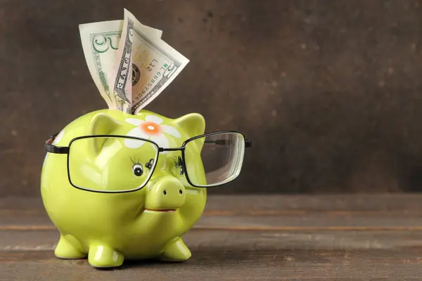 green pig piggy bank and money on brown wooden table, money saving concept.