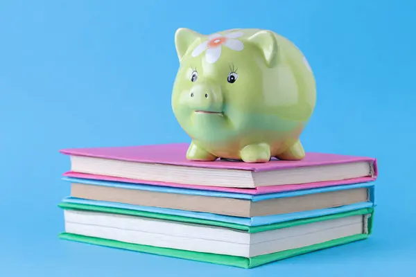 green pig piggy bank stands on books on a blue background, concept of saving money, saving for education