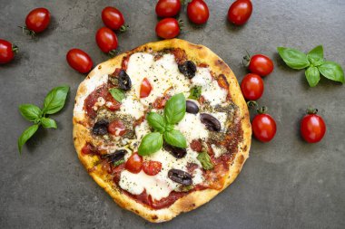 Mozzarella, Kalamata zeytinleri, kiraz domatesleri ve taze fesleğenli ev yapımı pizza.