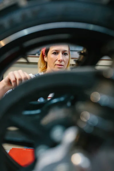 工場でオートバイのディスクブレーキを修理そばかすと女性の整備士 背景の女性に焦点を当てる — ストック写真
