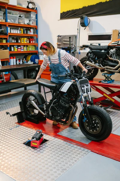Mechanic woman placing custom motorcycle over platform on factory