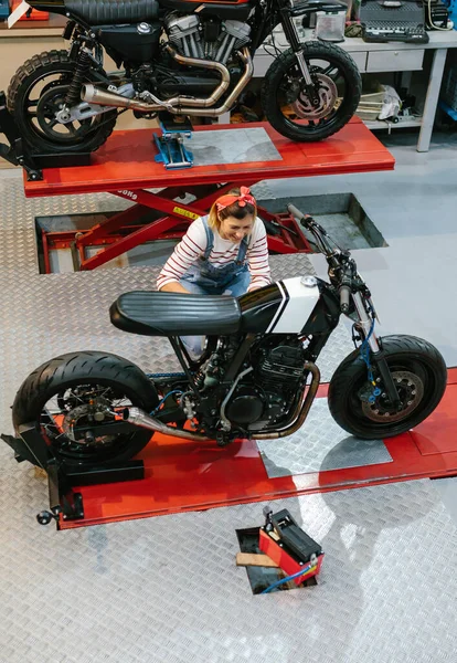 Smiling mechanic woman reviewing custom motorcycle on factory