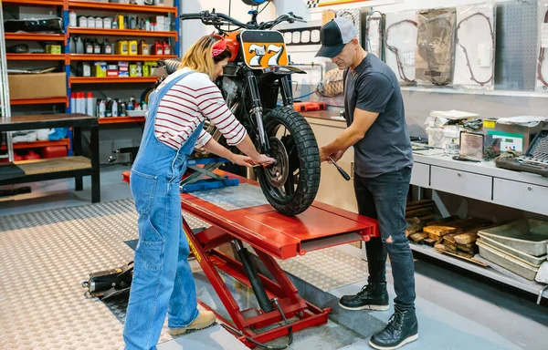 Mechanic couple team adjusting motorbike wheel over platform on factory