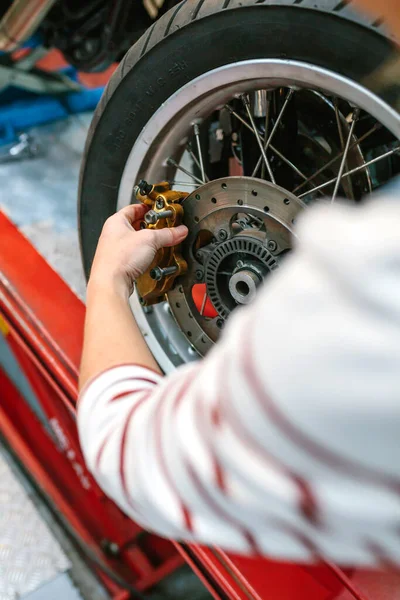 Close up of unrecognizable mechanic woman changing caliper brake system in motorbike wheel on workshop