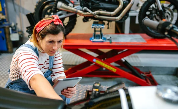 Mecânico Feminino Concentrado Com Tablet Digital Revisando Informações Motocicleta Garagem — Fotografia de Stock
