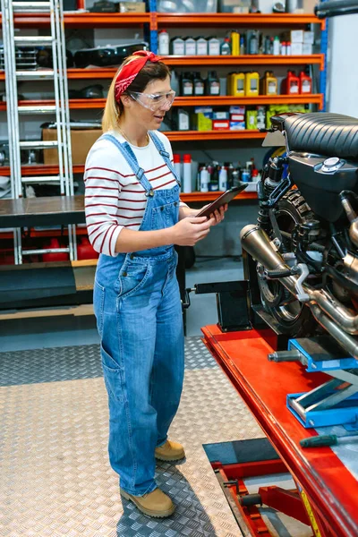 ガレージでオートバイのドキュメントをレビューしながら セキュリティメガネはデジタルタブレットを保持している女性整備士 — ストック写真