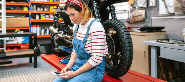 笑顔機械工の女性の肖像彼女の手で座っています上のプラットフォーム上でカスタムバイクで工場 — ストック写真