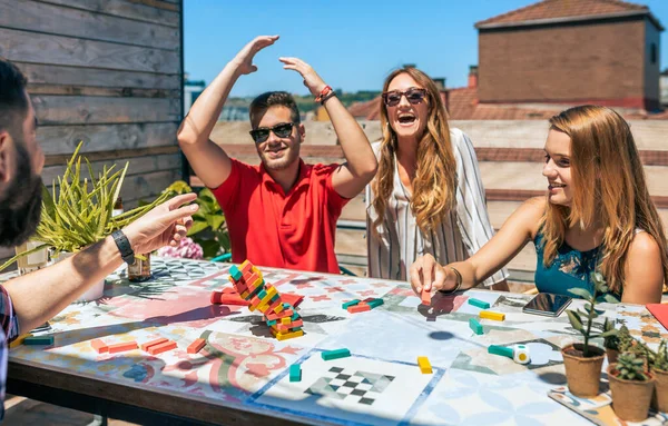 幸せな友人のグループが笑っている間若い男は夏に屋上パーティーでJengaゲームで失う — ストック写真