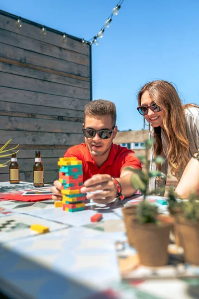 若いです男ともにサングラスプッシュJengaゲーム作品隣に彼の女性の友人に屋上で夏パーティー — ストック写真