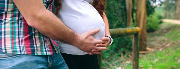 无法辨认的拉丁女性怀孕和她的伴侣抱着肚子在大自然中 — 图库照片