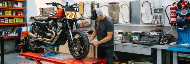 Tanımlanamayan tamirci, fabrika platformunda özel motosiklet motorunu kontrol ediyor.