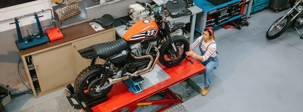 공장의 위에서 오토바이를 검토하고 기계공 여자의 — 스톡 사진