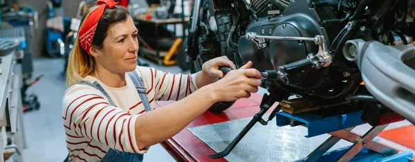 工場上のプラットフォーム上でオートバイのエンジンをレビューツールと幸せな整備士の女性の肖像画 — ストック写真