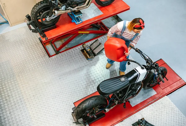 机修工女装塑料球衣的头像可在工厂平台上充填定制摩托车燃料箱 — 图库照片