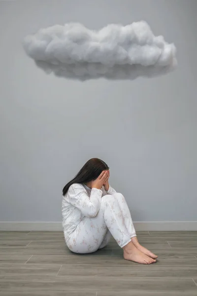 Unrecognizable woman with mental disorder and suicidal thoughts holding her head with hands sitting under a dark cloud on her room. Negative emotions and bad feelings concept.