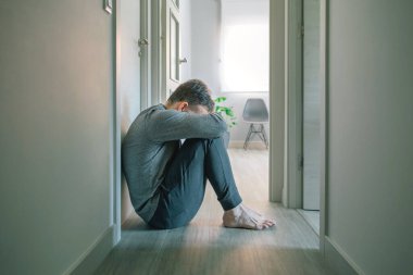 Unrecognizable man in pajamas with mental disorder and suicidal thoughts crying sitting on the floor of a mental health center clipart