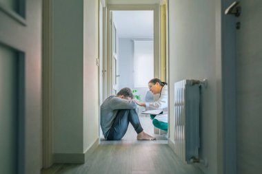 Kadın doktor koridorda oturan erkek hastaya empati kurup yardım ediyor.