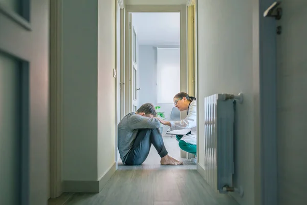 女医は安心して廊下の部屋の床に座っている男性患者への共感を助ける — ストック写真