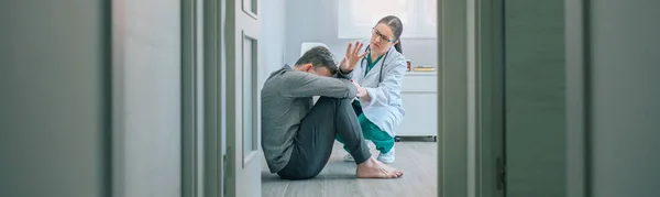 女医生试图帮助那些拒绝帮助坐在精神科病房地板上的精神障碍男性患者 — 图库照片