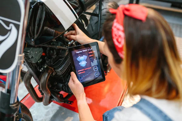 无法辨认的机修工妇女在工厂使用数字平板电脑中的发动机诊断应用程序来查看摩托车 — 图库照片