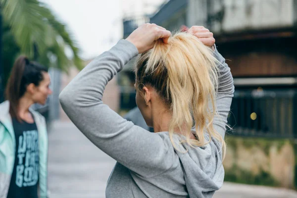 在训练前 无法辨认的金发女跑步者把她的头发绑在女性朋友旁边的马尾辫上 — 图库照片