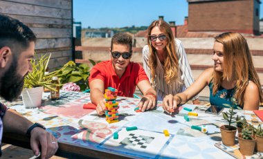 Bir grup mutlu ofis çalışanı kahve molasında terasta Jenga oyunu oynuyorlar.