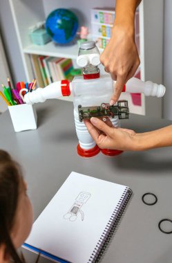 Tanımlanamayan bayan öğretmen öğrencilerine plastik paketlerle yapılmış geri dönüşümlü oyuncak robotların elektrik devrelerini nasıl bağlayacaklarını anlatıyor. Sürdürülebilir teknolojik eğitim kavramı.