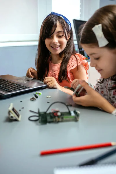 stock image Portrait of happy female student smiling while looking to classmate assembling machine pieces in a robotics class. Elementary technological education concept.
