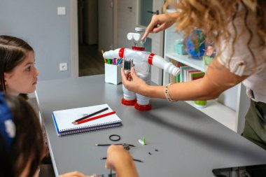 Öğrencilerine plastik paketlerle yapılan geri dönüşümlü oyuncak robotun üzerinde güneş paneli gösteren bir robot kadın öğretmen. Sürdürülebilir teknolojik eğitim kavramı.
