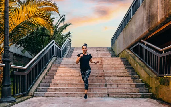 幸せな若い女性ランナーは 日没にヤシの木と都市滑走路の階段をトレーニング — ストック写真