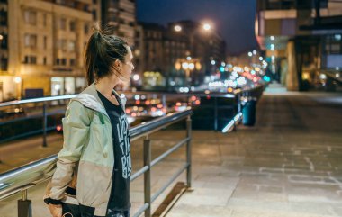 Tanımlanamayan, at kuyruklu esmer kadın koşucu, geceleri boş bir kasabada antrenman yapmadan önce bacaklarını tırabzanın yanına uzatıyor.