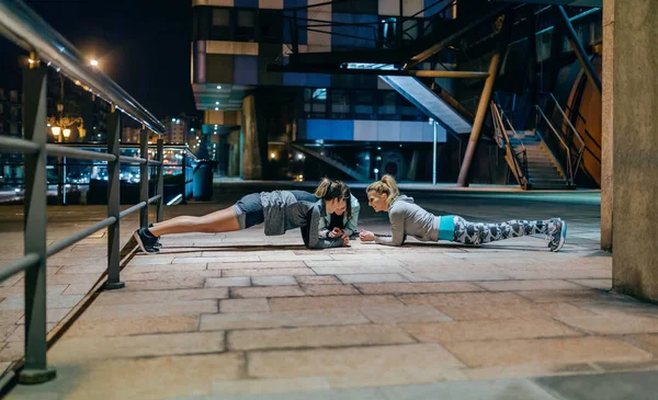 年轻女性朋友们晚上在空旷的城市一起训练时 一边练木板一边玩耍 — 图库照片