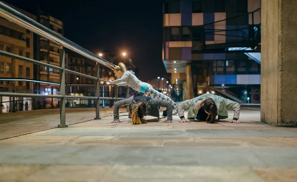 Female young friends sport team doing push ups during training together on the empty city at night
