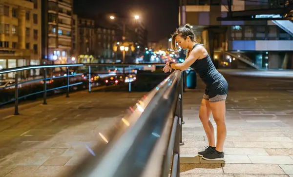 若い金髪ランナーの女性は 町で夜にトレーニングした後 スマートウォッチアプリケーションで運動の進行状況をチェックします 女性アスリートの休憩と健康アプリの心拍数モニター 左コピースペース — ストック写真
