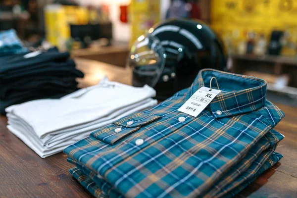 Close up of label with price and size over a blue plaid shirt on industrial style store. Organized apparel stacks over counter ready to sell on vintage clothes shop. Clothes small business concept.