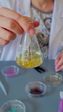 Tanımlanamayan kadın kimyager teknisyen Erlenmeyer şişesini, çevre araştırma laboratuvarında altın parıltı örneğiyle sallıyor. Avrupa Birliği 'nin mikroplastik kullanımını yasaklama kavramı.