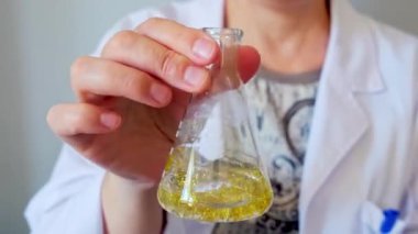 Çevre araştırma laboratuvarında, tanınmayan kadın kimyacı teknisyenlerin el sıkışarak Erlenmeyer şişesini altın parıltı numunesiyle sıkarak kapatın. Avrupa Birliği 'nin mikroplastik kullanımını yasaklama kavramı.