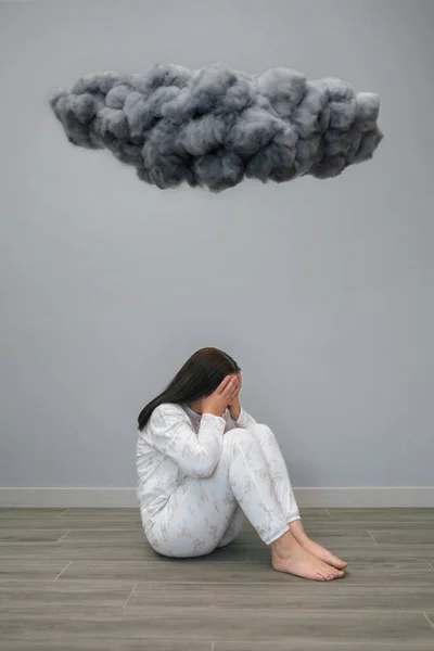 Unrecognizable desperate woman with mental health problems covering her face with hands under a dark storm cloud on her room. Negative emotions and bad feelings concept.