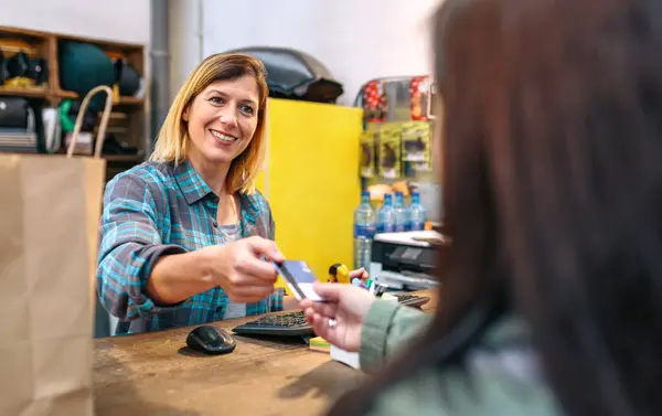 笑顔の金髪女性ショップアシスタントは 購入を請求するクライアントのクレジットカードを取ります ヴィンテージストアで女性のお客様にサービスを提供する陽気な女性キャッシャー 中小企業 地域商業コンセプト — ストック写真