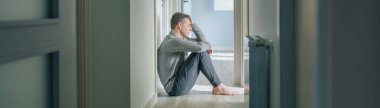 Desperate man with mental disorder and suicidal thoughts holding his head with hand sitting on the floor of a mental health center clipart