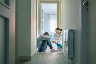 Kadın psikiyatrist, koridorda oturan akıl hastası ve intihara meyilli erkek hastayla konuşuyor.