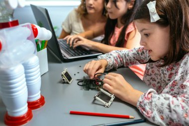 Okul çocuğu robotik dersinde öğretmeniyle dizüstü bilgisayar kullanırken elektrik devresinden tel bağlayan kız öğrencinin portresi. Sürdürülebilir teknolojik eğitim kavramı.