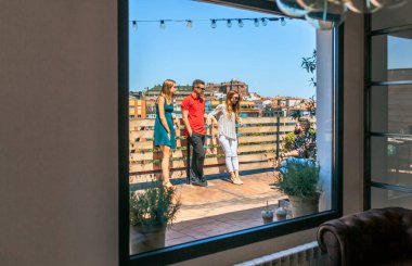 Bir yaz günü arkadaş grubunun şehir çatısı ve dinlenme odasının penceresinden konuşmalarının görüntüsü