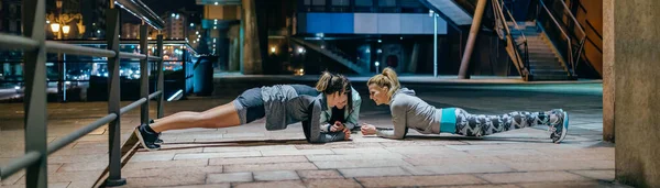Young women friends sport team having fun while doing plank exercise during training together on the empty city at night