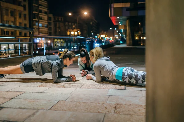 Young women friends sport team doing plank exercise during training together on the empty city at night