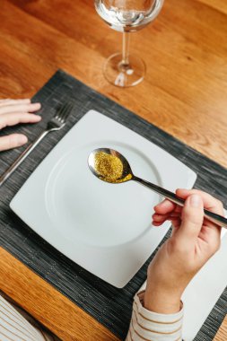 İnsanlara ve çevreye zararlı plastiklerden oluşan bir kaşık dolusu altın parıltıyı elinde tutarak yemeye hazır, tanınmayan bir kadının olduğu yakın plan. Avrupa Birliği 'nin mikroplastik kullanımını yasaklama kavramı.