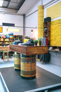 Boş bir ikinci el giyim mağazasının tepesinde giysi yığınları olan yakıt varilleri tarafından desteklenen ahşap tezgahı kapatın. Retro giyim mağazasının içi. Sürdürülebilir alışveriş ve dairesel ekonomi