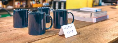 Yerel dükkandaki ahşap tezgahın üzerinde endüstriyel dekorasyonlu mavi bardaklar. Masada indirimli makaleleri olan boş bir retro dükkanının içi. Küçük işletme konsepti. İnsan Yok.